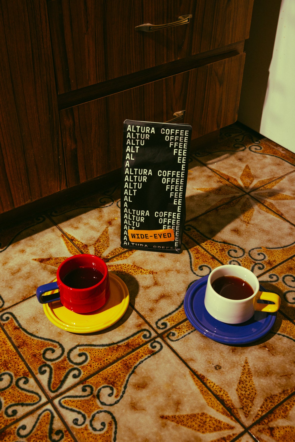 Altura Coffee Wide-Eyed espresso blend bag with two cups of coffee on patterned tiles